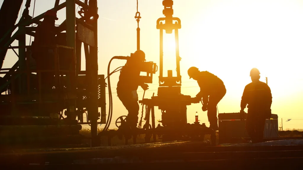 Silhouette of maritime workers operating heavy machinery at sunset.
