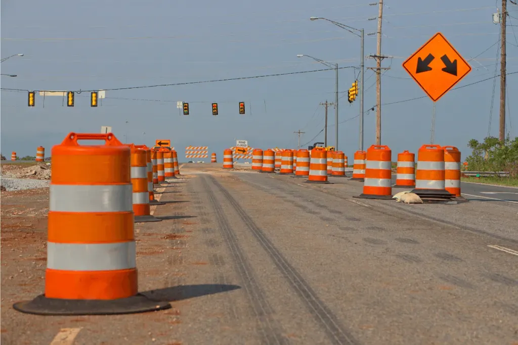 A road under construction with orange traffic barrels and warning signs.