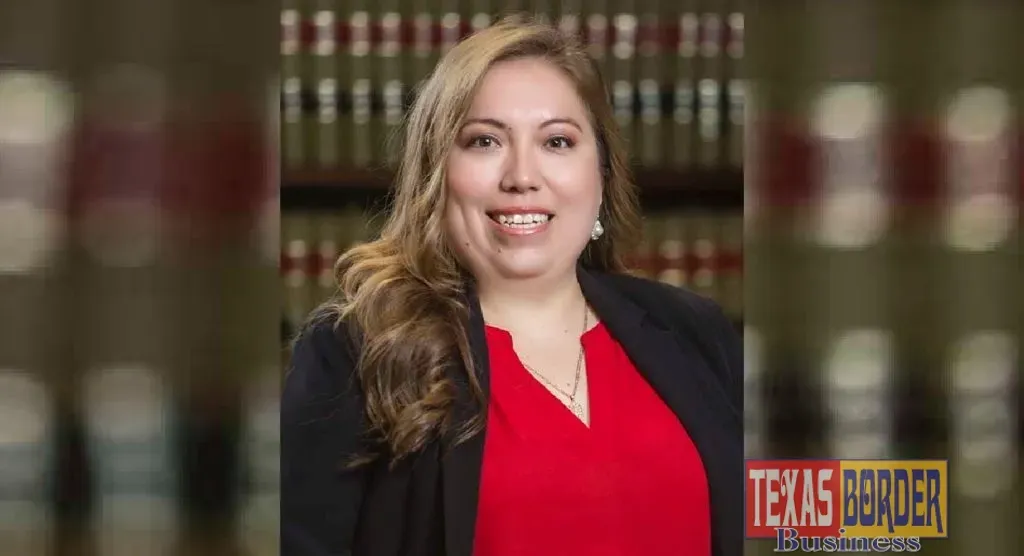 A smiling woman lawyer in a black blazer and red top, in front of a blurred law bookshelf.