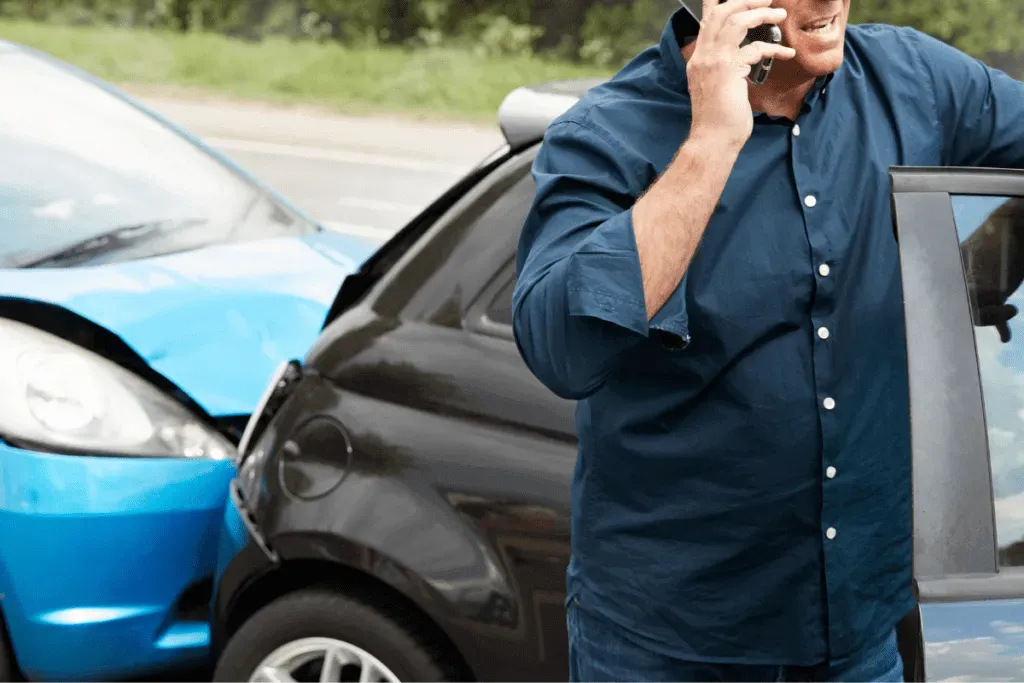 a man talks on a cell phone while standing outside his car next to a two-car rear-end accident.