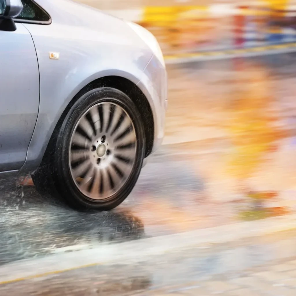 Close-up of a silver car tire spinning rapidly and splashing water on a wet, motion-blurred street.
