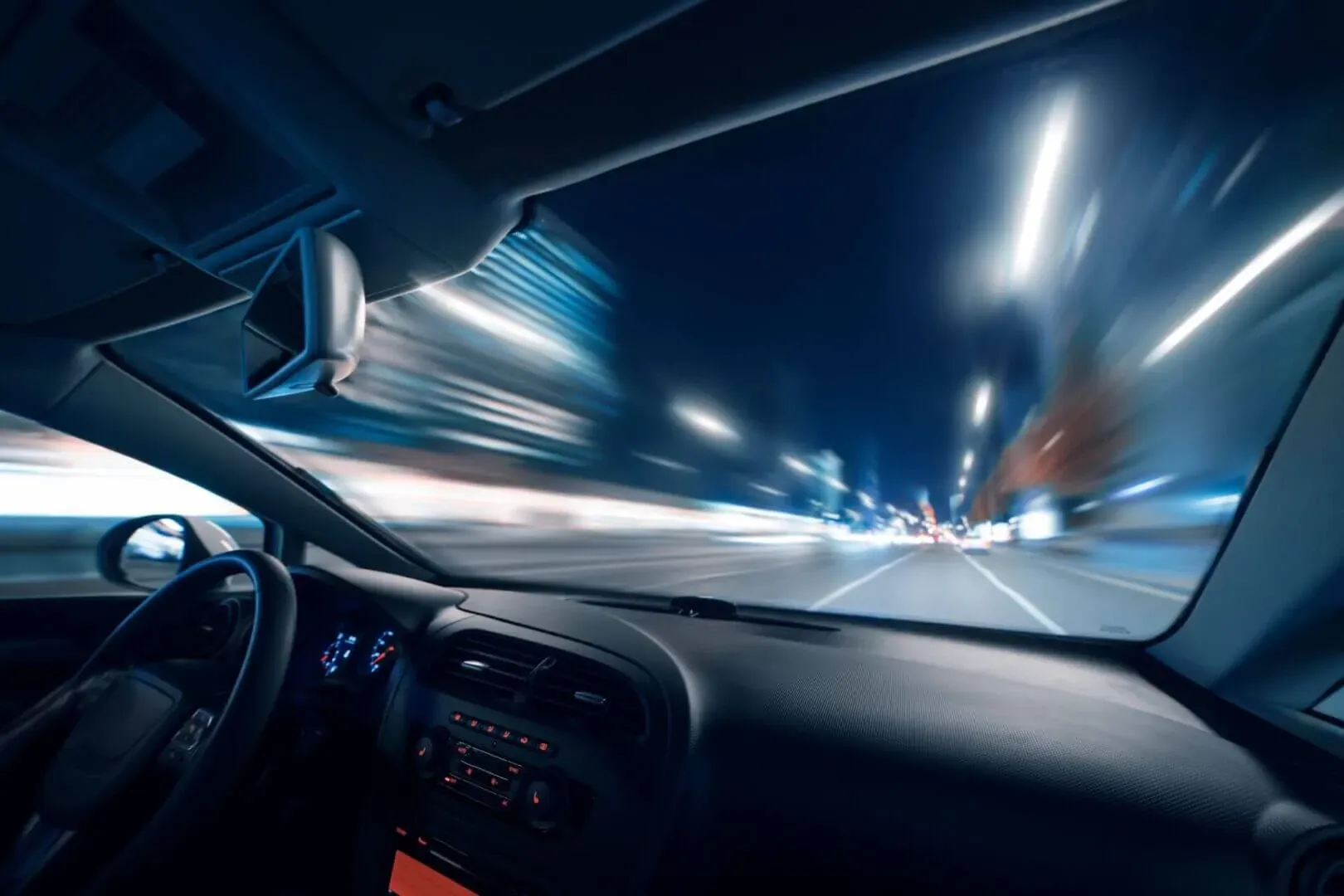 shows an interior view from inside a car driving at night, featuring a motion-blurred city street ahead.