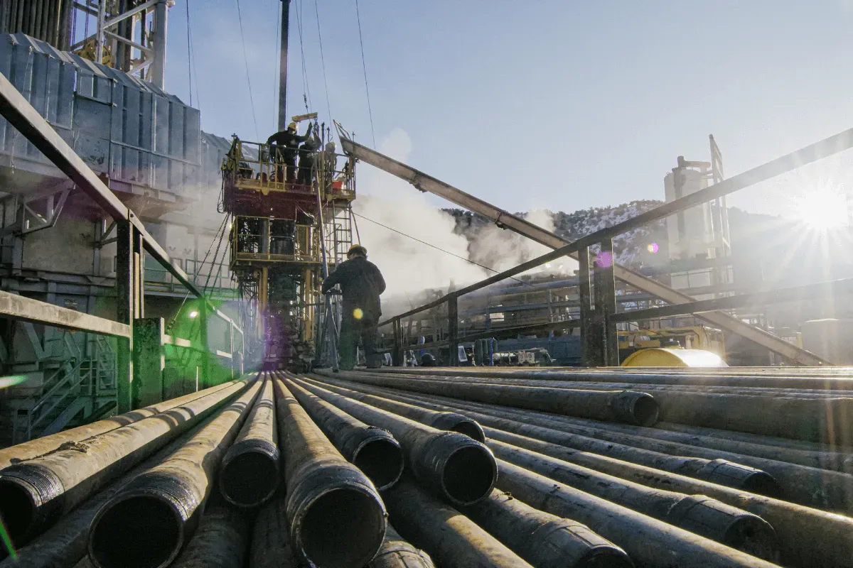 The file shows an active industrial drilling rig with workers operating machinery, featuring large metal pipes laid out in the foreground under bright sunlight.