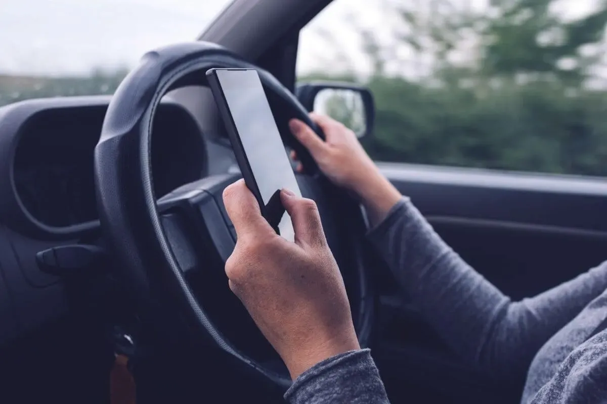 A driver holding a smartphone while keeping one hand on the steering wheel of a moving car.
