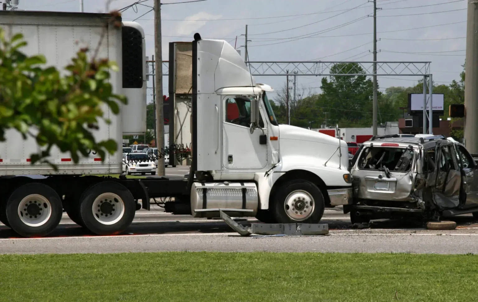 A white semi-truck crashed into the rear and side of a severely damaged silver SUV on a road.